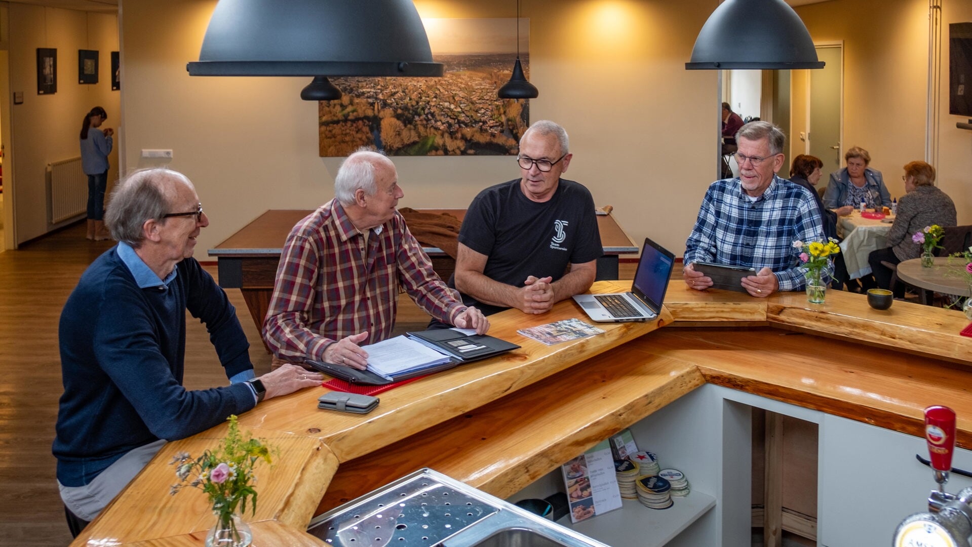 Jaap Diepeveen en Joost Nachbahr in gesprek met een buurtsportcoach en een vrijwillige medewerker van het wijkcentrum.aan de bar van De Kruisdam. 
