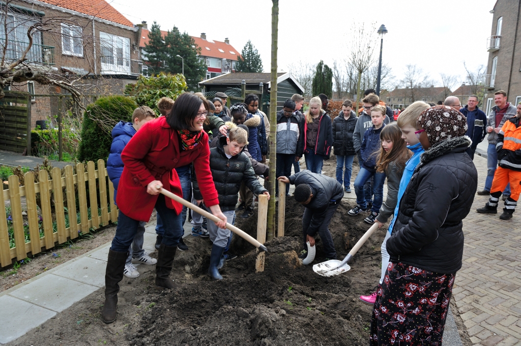 Wethouder Van der Mark helpt kinderen met het planten van bomen.