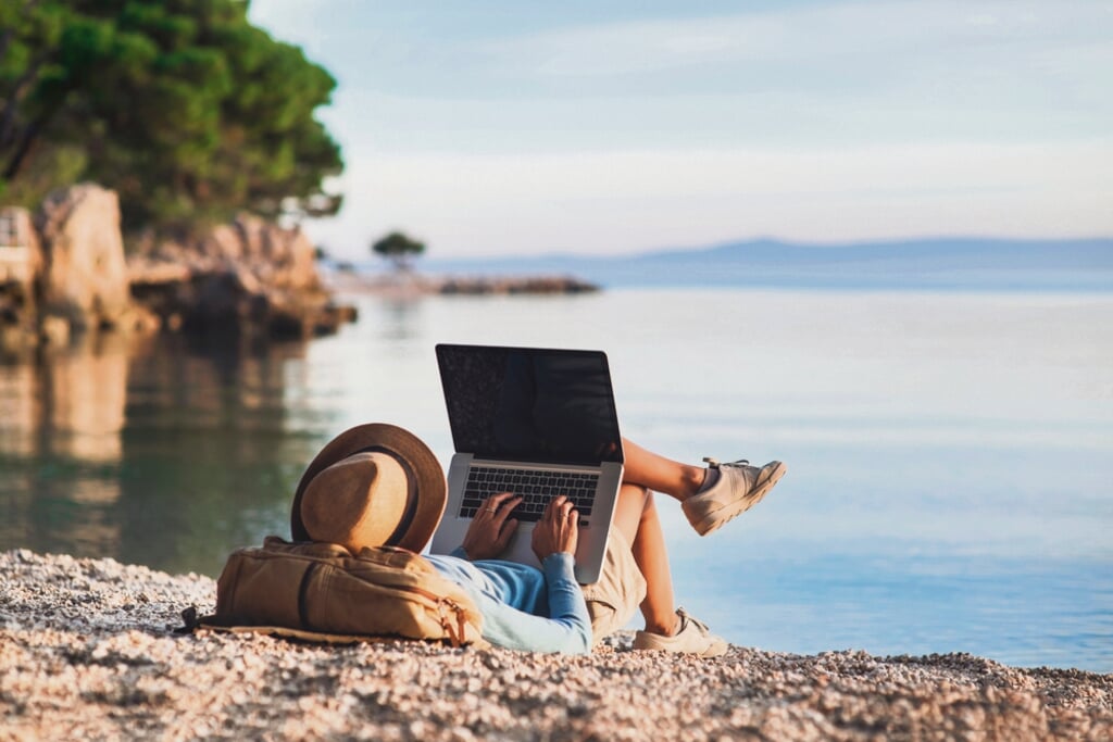 Young woman using laptop computer on a beach. Girl freelancer working by the sea. Freelance work, travel, vacations, stay connected, communication, studying online, e-learning concept