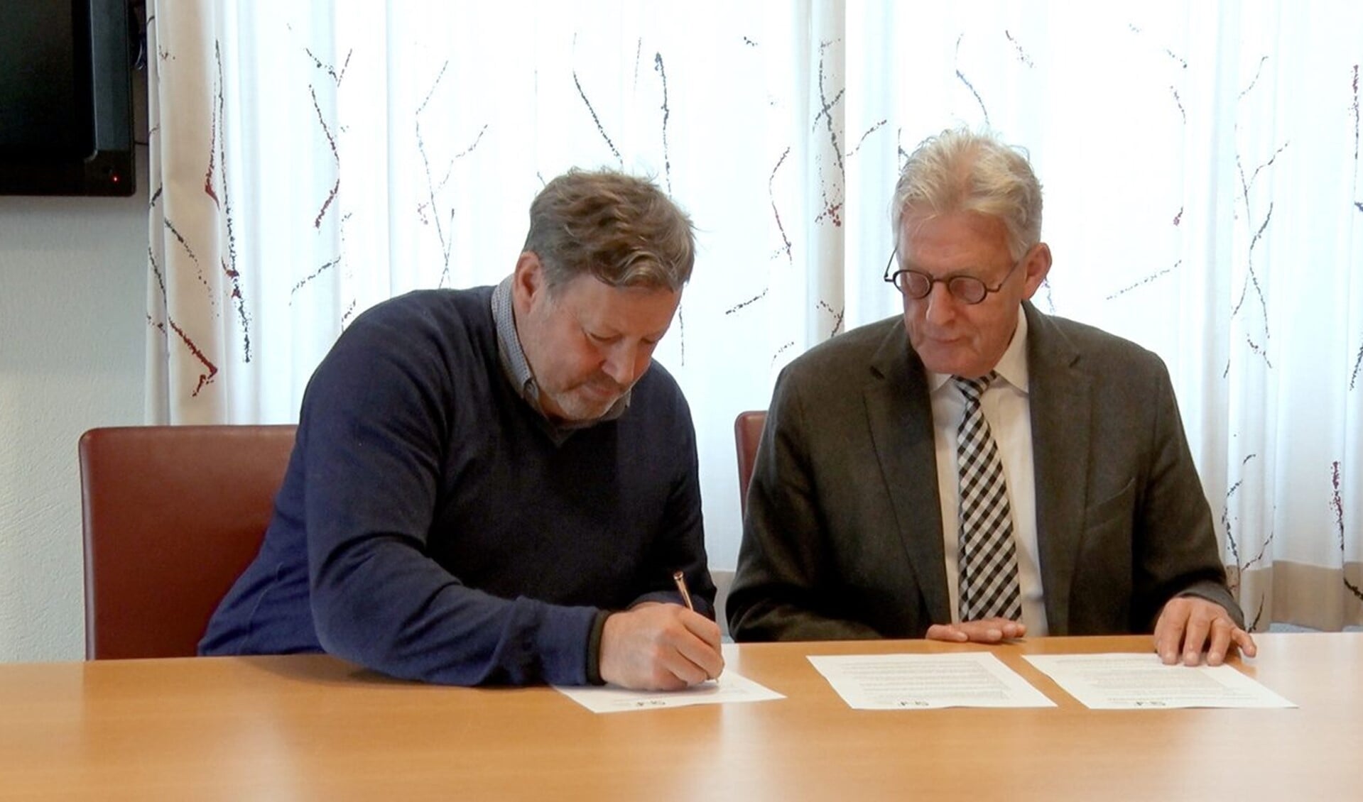 Wethouder Louis Swinkels (l) tekent het convenant. Rechts voorzitter van Stichting Normering Flexwonen, Koos Karssen. (Foto: Siris-tv)