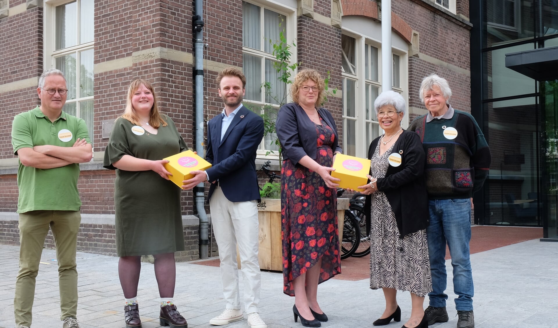 Wethouder Tom Oomen en burgemeester Greet Buter (in het midden) ontvangen de Fairtrade-box uit handen van Kernteam Fairtrade: Michel Lintermans, Jannine Brugman-Meijer, Lieve Glas en Lambert van Lieshout.