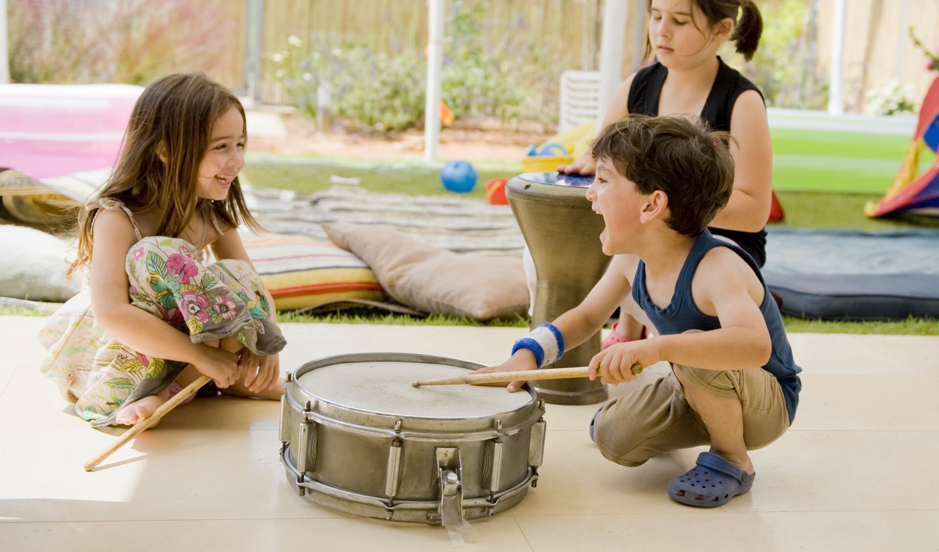 three kids in the backyard having fun with drums.