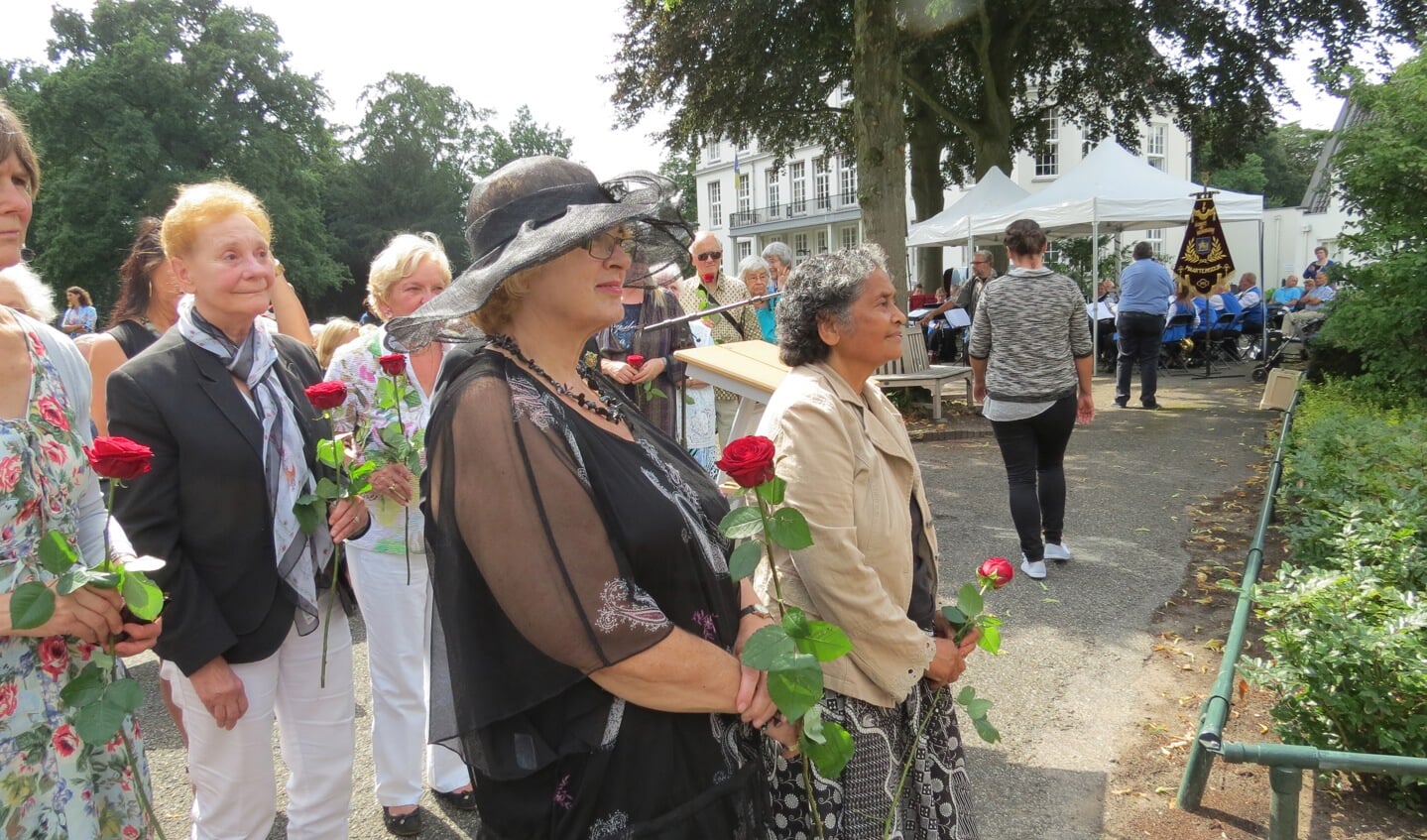 Zeventig aanwezigen plaatsen een rode roos in vazen bij het monument.