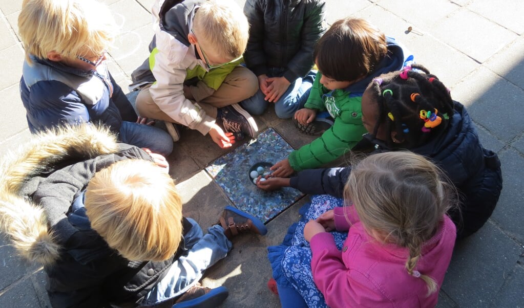 Kinderen van groep 1 spelen bij een knikkertegel van gerecycled plastic.