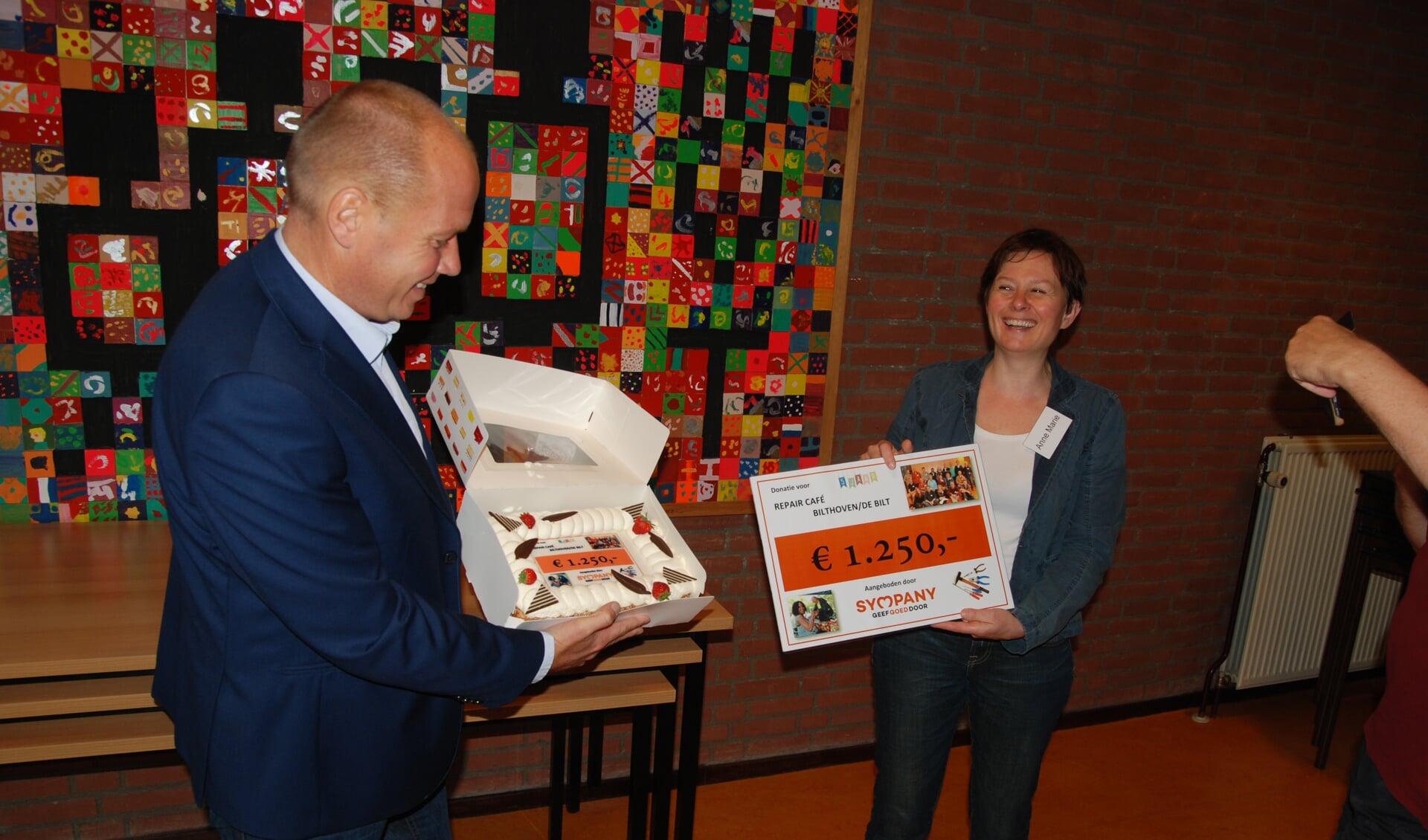 Anne Marie Gout, organisatrice van Repair Café Bilthoven, ontvangt uit handen van Martijn van Veenendaal de gulle gift van Sympany. Voor bij de koffie van de vrijwilligers bracht hij een heerlijke slagroomtaart.