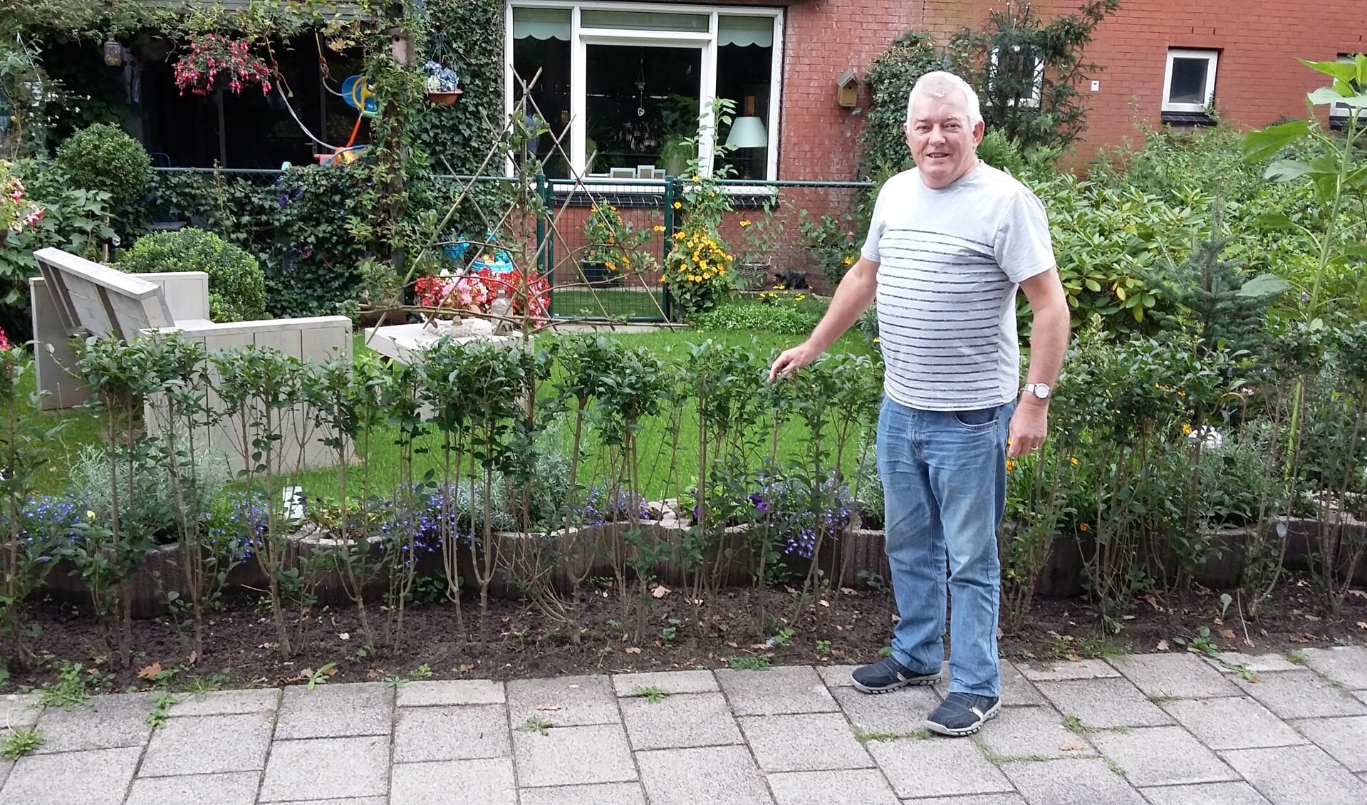 Pieter Pols voor zijn fraaie tuin met bloemen, gras en bank.