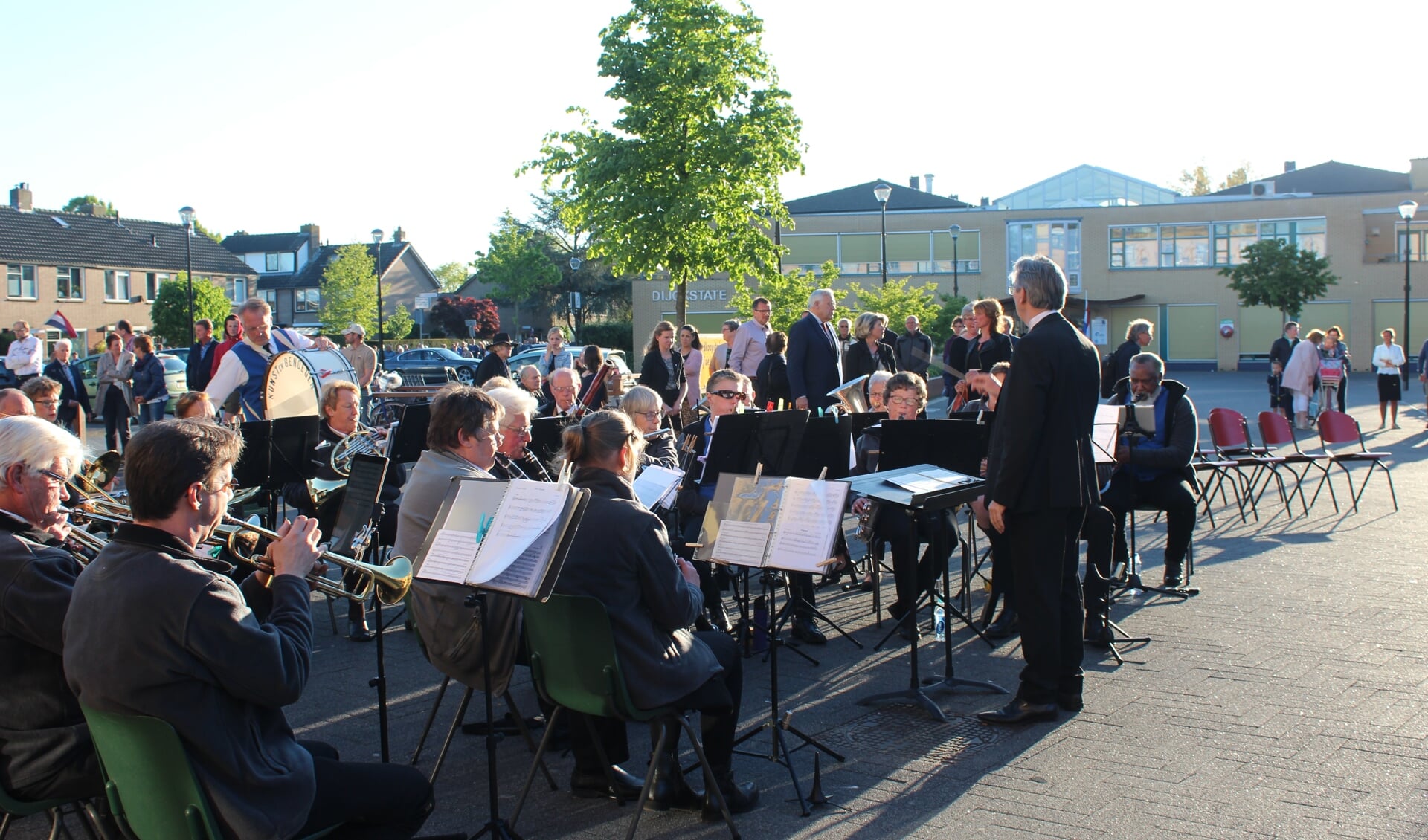 Het gezelschap bereikt het Maertensplein, waar muziekvereniging Kunst en Genoegen bij de vlag koralen speelt. 