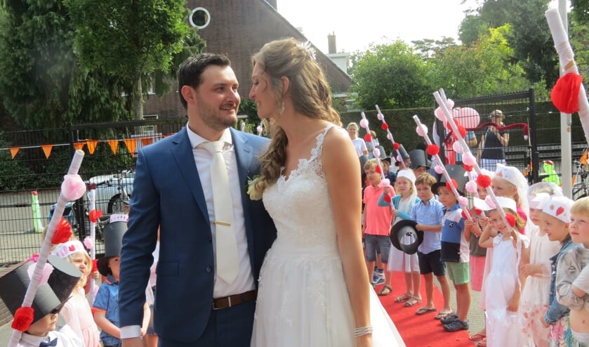Het bruidspaar wordt door alle groepen van de school enthousiast verwelkomd en toegejuicht.