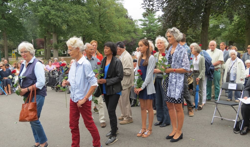 Drieënzeventig aanwezigen plaatsen een rode roos in vazen bij het monument.