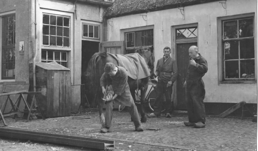 De jonge Geurt Vervat beslaat een paard, terwijl vader Goossen Vervat (rechts) toekijkt. (foto familie Vervat)