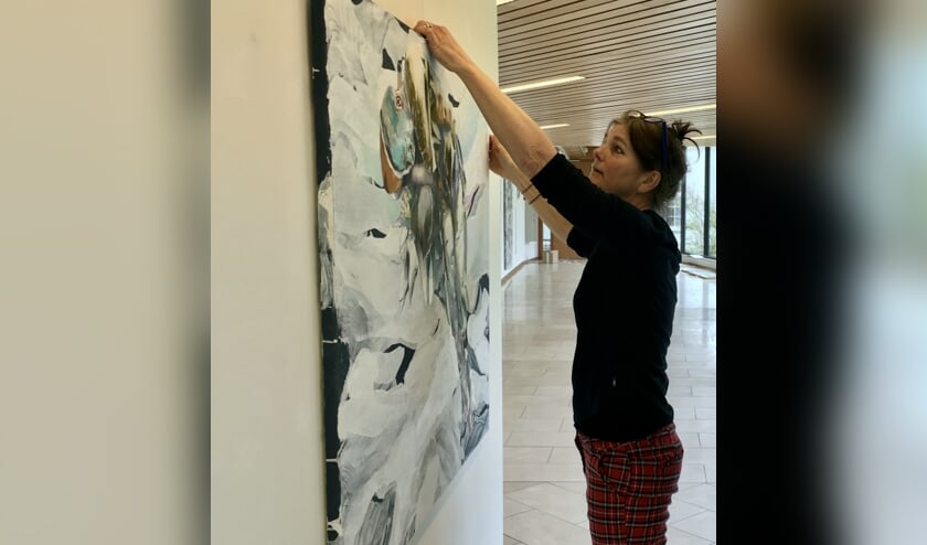 Lilian Oldenhof hangt een schilderij op van Kars Persoon in de traverse van het gemeentehuis. (foto Katrien Kroes)