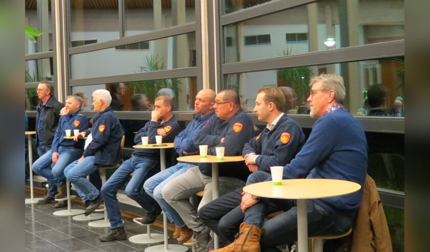 Brandweerlieden op de publieke tribune luisteren mee naar de antwoorden van de burgemeester op vragen over een redvoertuig.