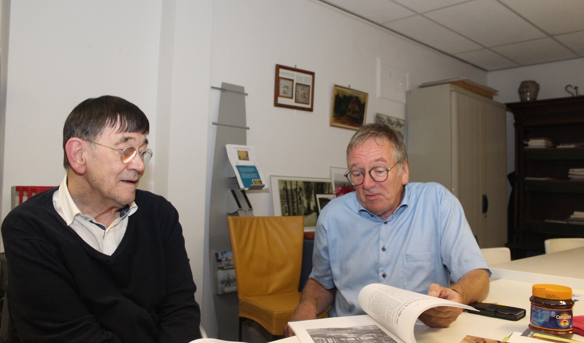 Koos Kolenbrander en Jan Maasen bladeren door de analoge verzameling van de Maartensdijkse dorpschroniqueur.