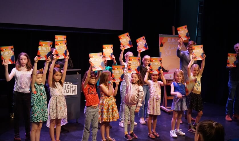 Kinderen van het koortje krijgen van wethouder Dolf Smolenaers het Kunst Doe Boek uitgereikt. krijgen.