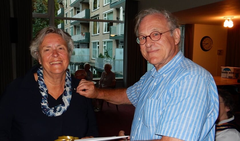 De zilveren speld wordt opgespeld door haar man die op de achtergrond altijd een ondersteunende rol heeft vervuld.