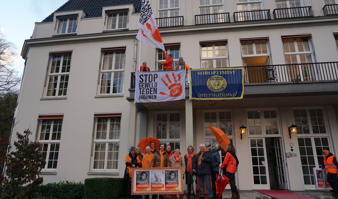 Enkele leden van de Soroptimisten hijsen de vlag tegen geweld hijsen op het balkon van het gemeentehuis. 