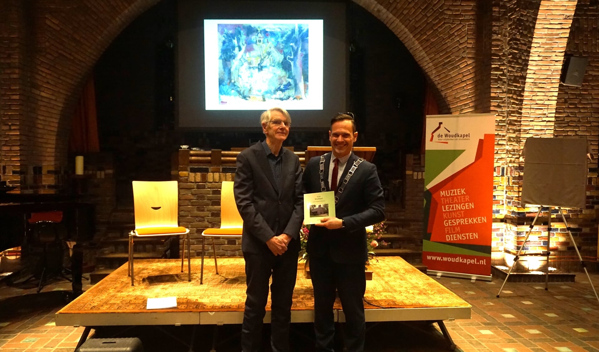 Burgemeester Sjoerd Potters ontvangt het eerste exemplaar van het boek ‘100 jaar Woudkapel’ uit de handen van auteur Otto Tissing.