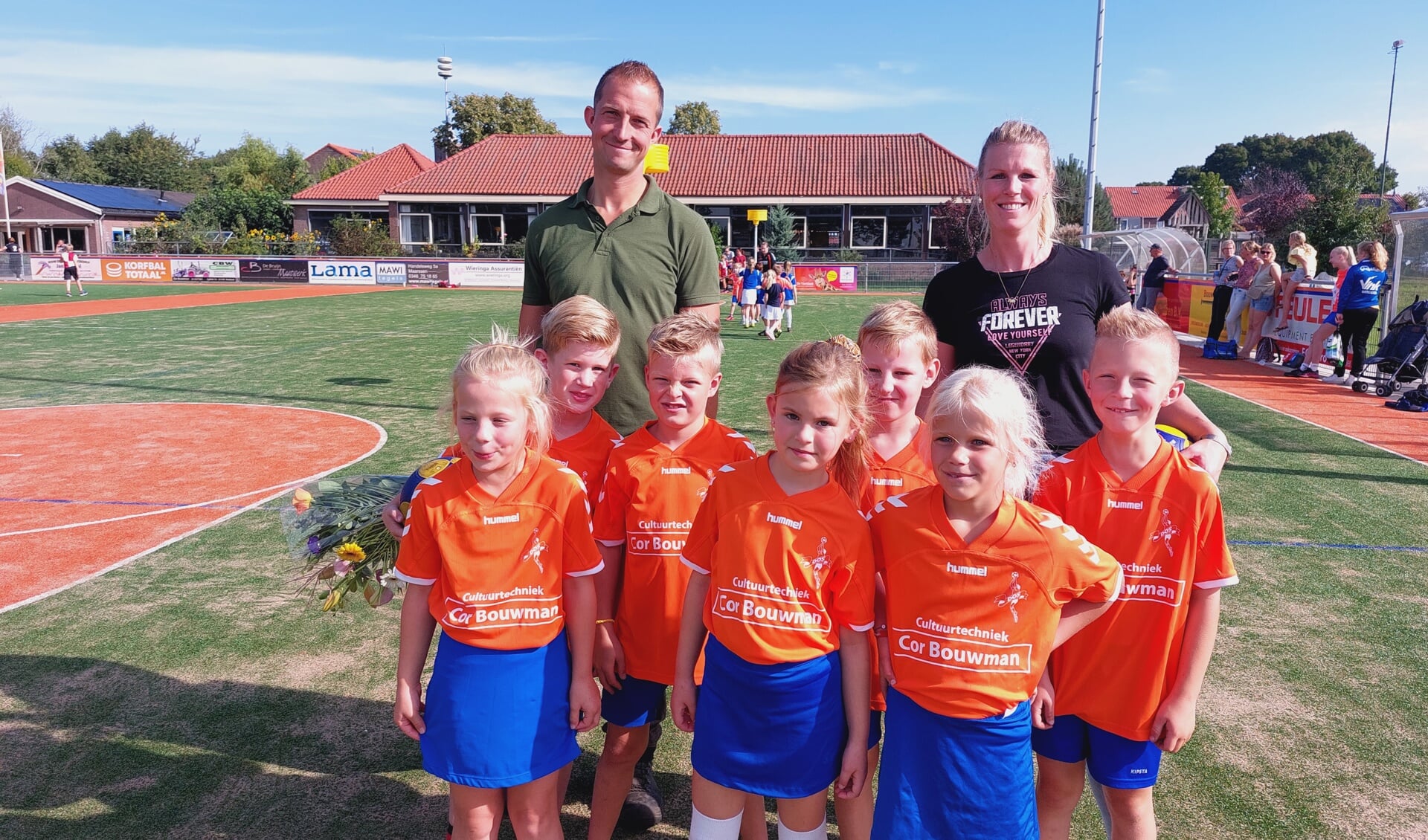 Cor Bouwman met bloemen en trainer/coach Marcella Bouwman met daarvoor de spelers in de nieuwe shirts.
