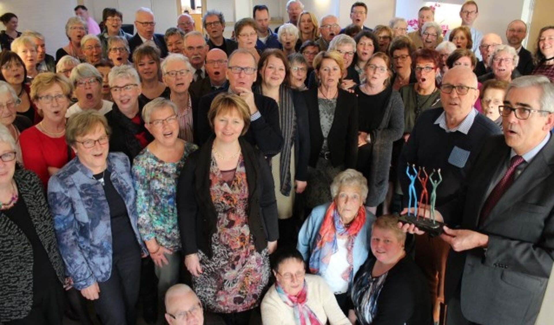 Samen 150 jaar: 100 jaar voor het koor en 50 jaar lidmaatschap van Kees Klein (tweede van rechts) naast voorzitter Beewukes met de sculptuur Applaus. FOTO: Lysette Verwegen