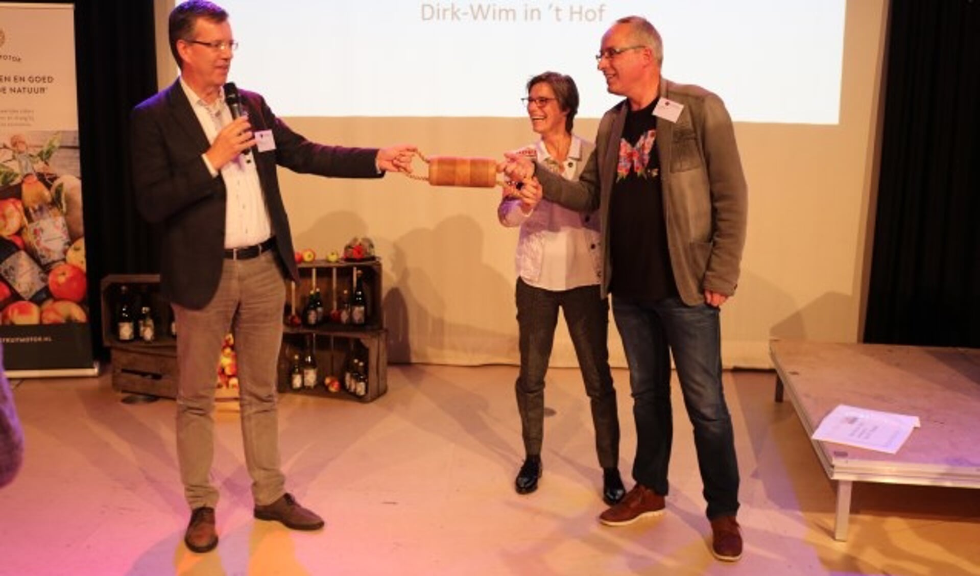 Joost Reus overhandigt het circulaire estafettestokje aan Hilde Engels en Henri Holster van De Fruitmotor