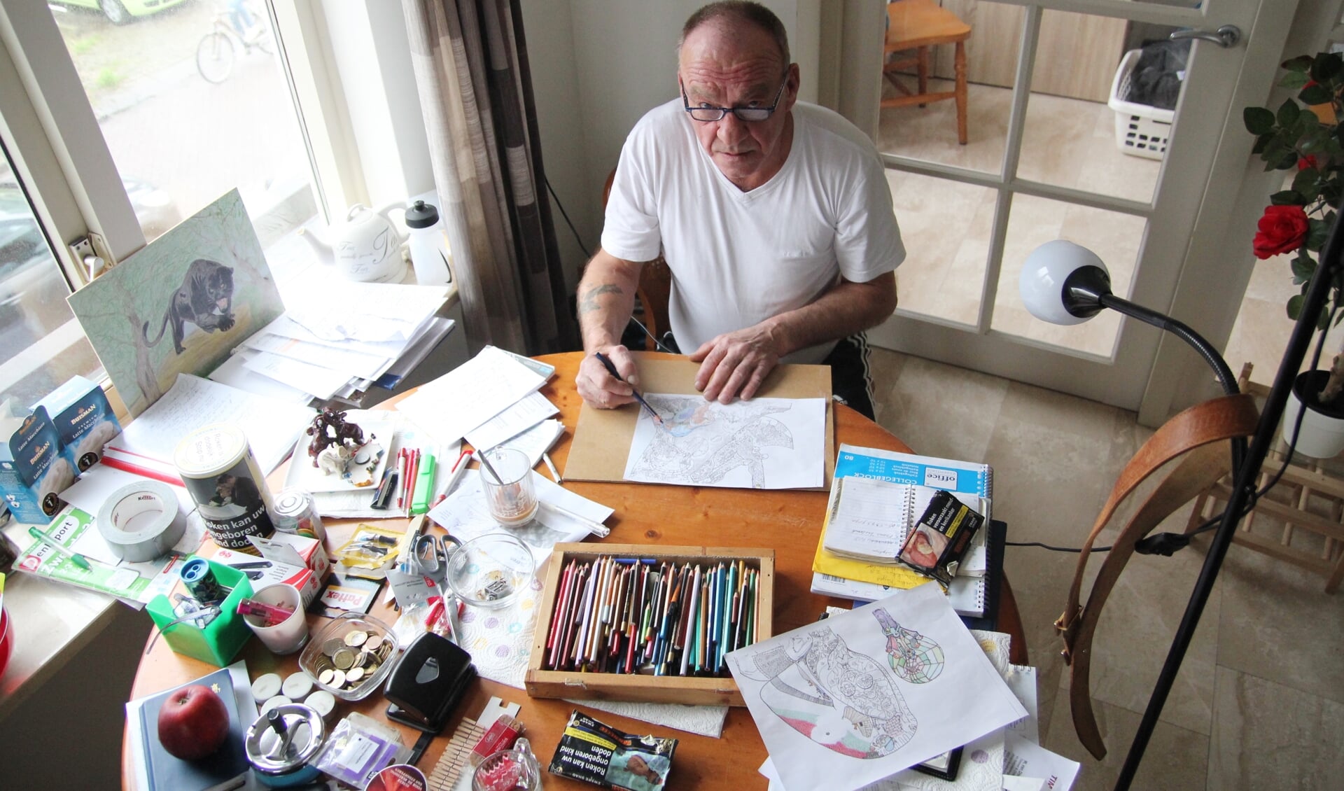 • Ad van Wijk aan zijn 'tekentafel', waar hij graag zit om tekeningen in te kleuren.