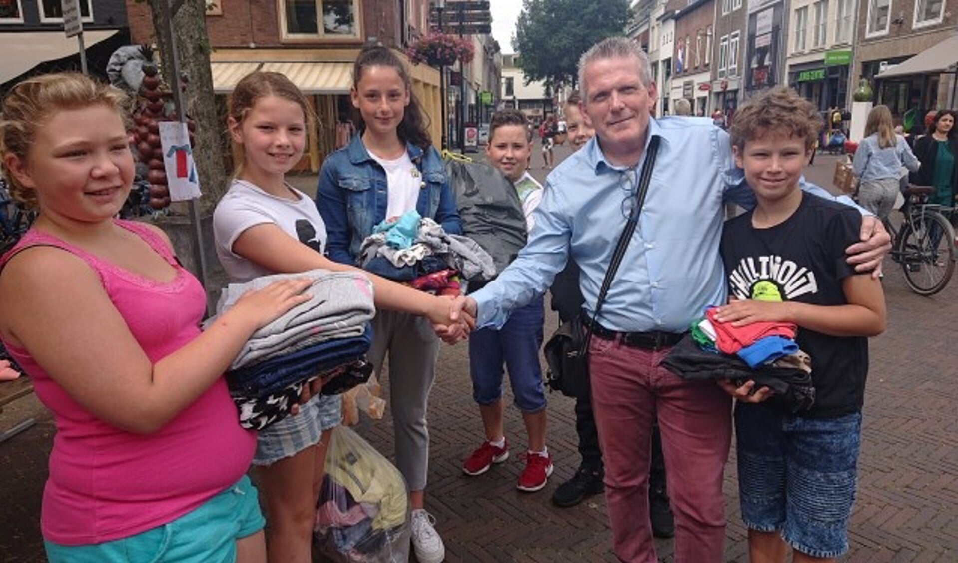 Mario van Keulen van stichting Klesteo ontvangt uit de handen van de Tielse kinderraad stapels met kleding.
