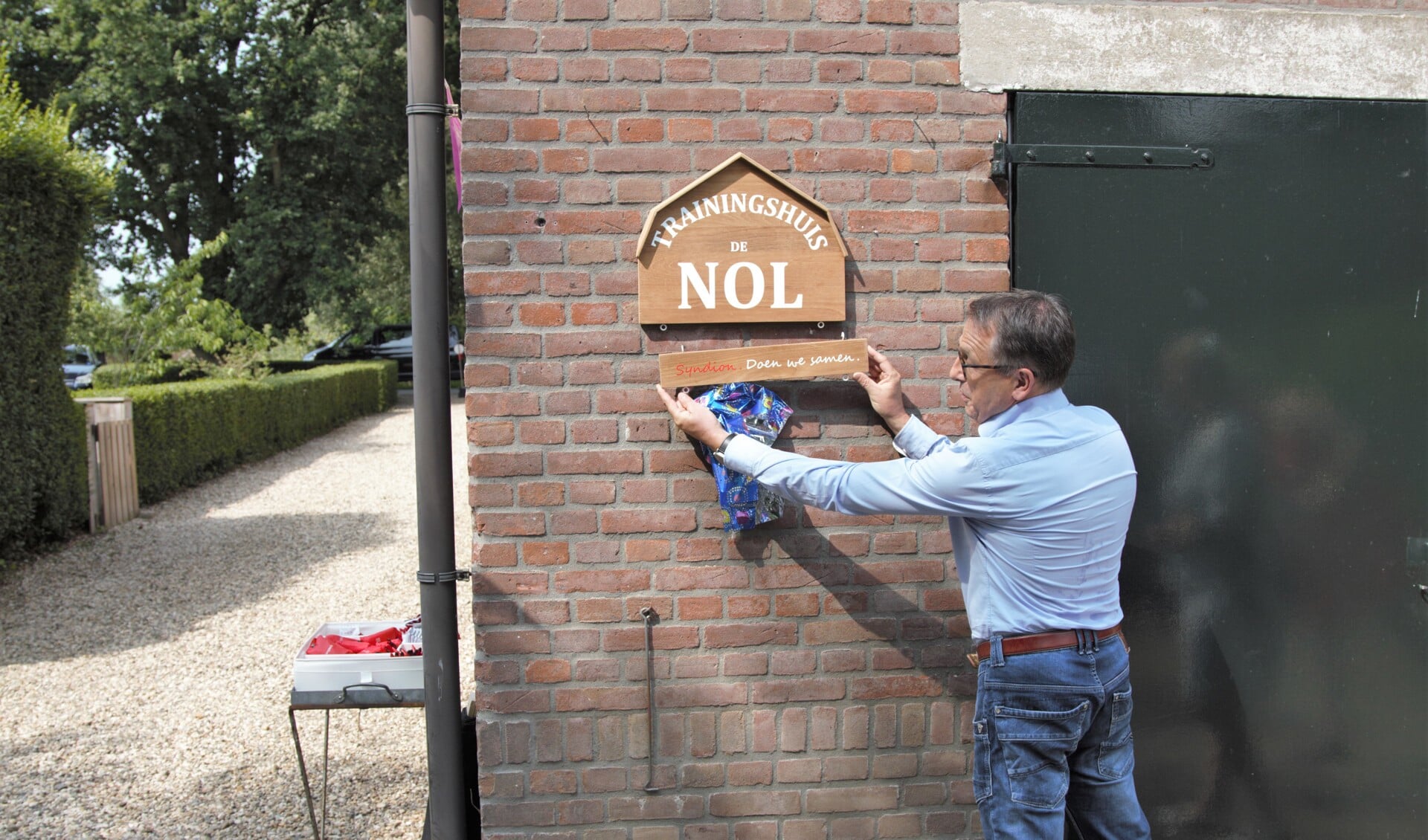 • Bestuurder Harry Vogelaar bevestigt het naambord bij de officiele opening van Trainingshuis De Nol.