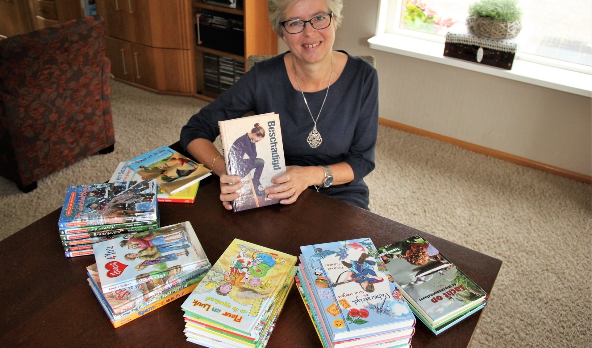 • Teunie Suijker met al haar boeken. In haar hand haar nieuwste boek: Beschadigd.