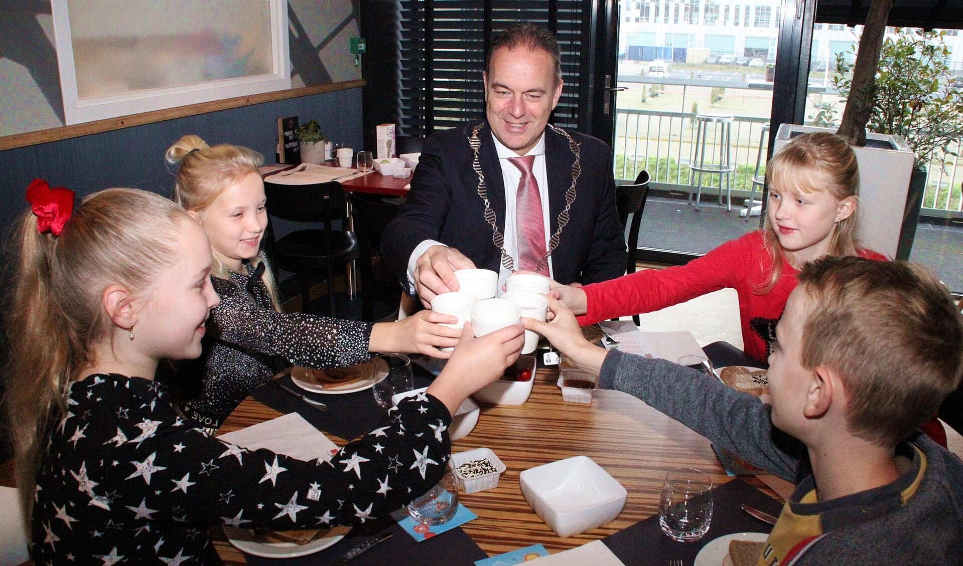 • De kinderen toasten met de burgemeester op het lekkere ontbijt. 