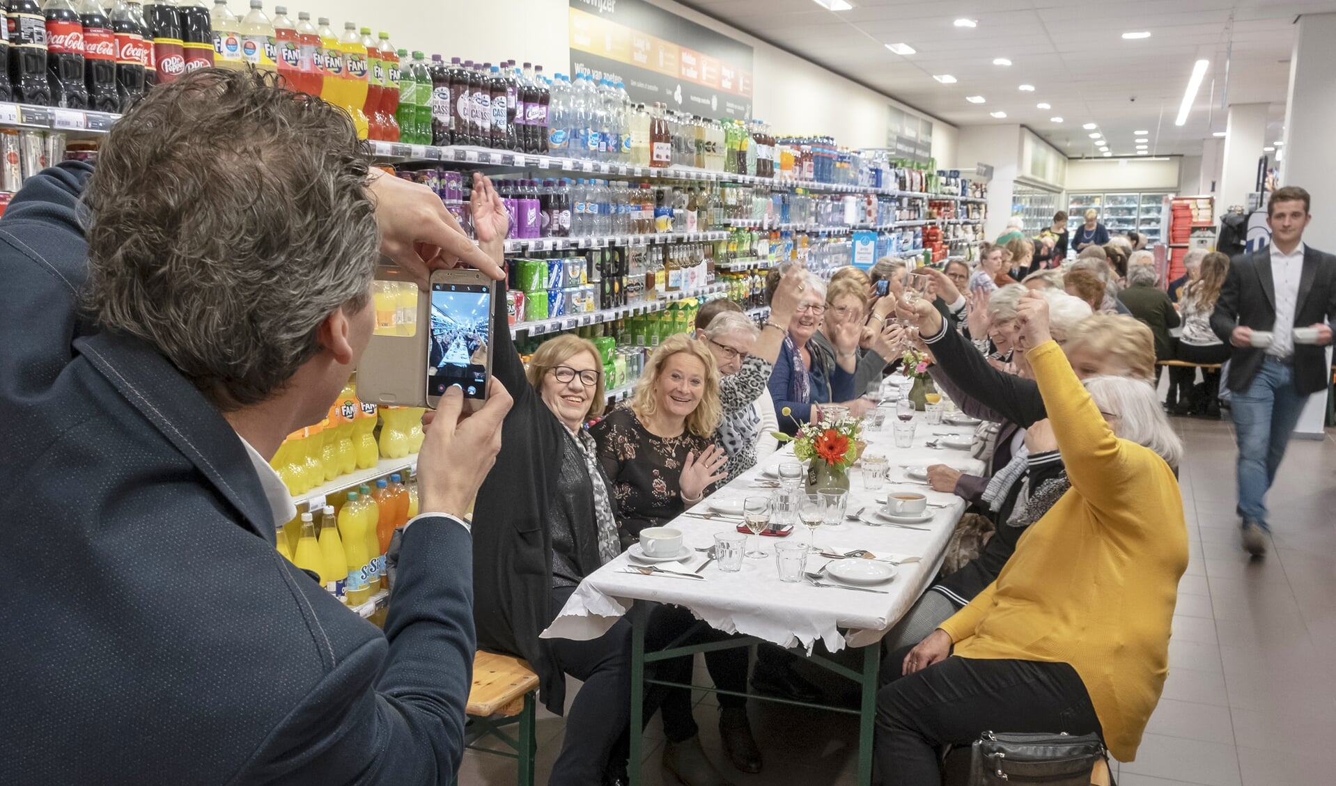 • Supermarkteigenaar Erik Wiersma van de Albert Heijn in Krimpen aan de Lek neemt een foto van de gasten die hun eten kregen geserveerd aan een lange eettafel. 
