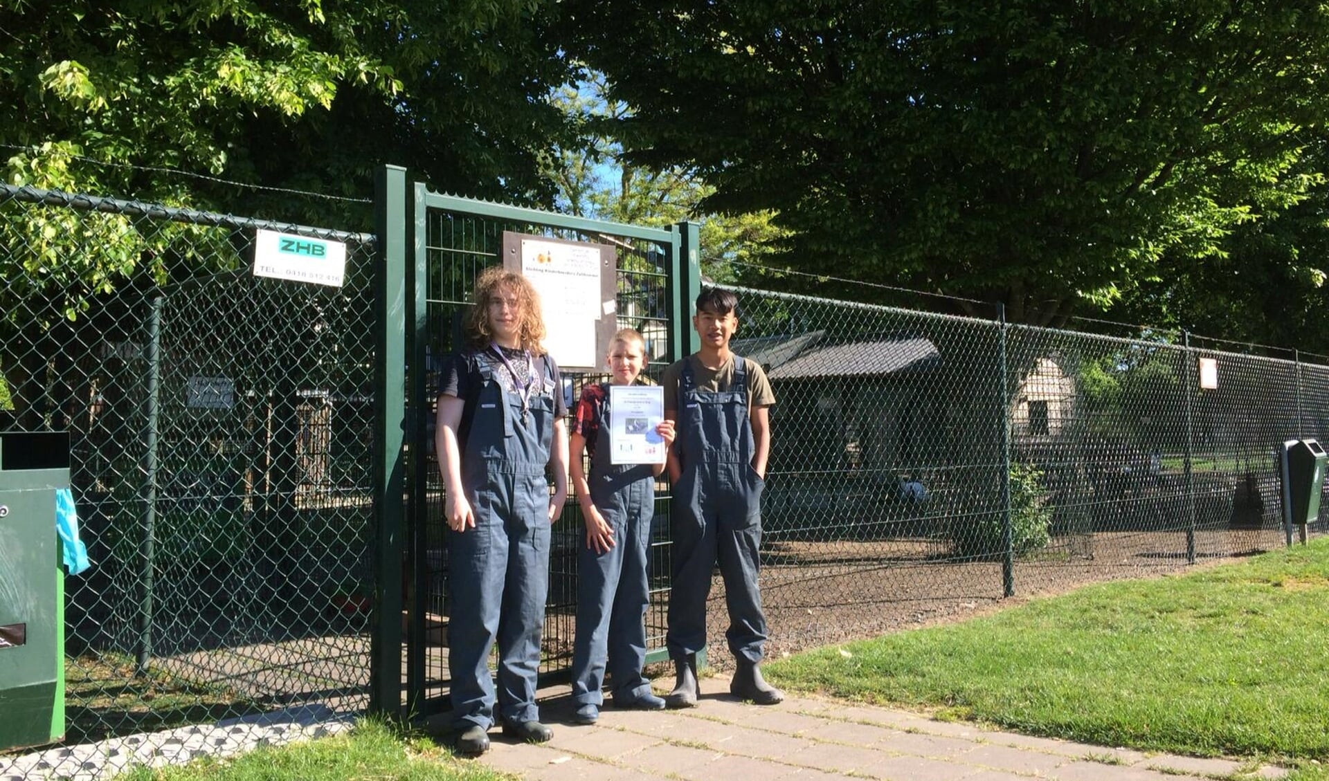 • Drie leerlingen van De Brug staan bij de kinderboerderij met het bewijs van adoptie van de dwerggeiten.