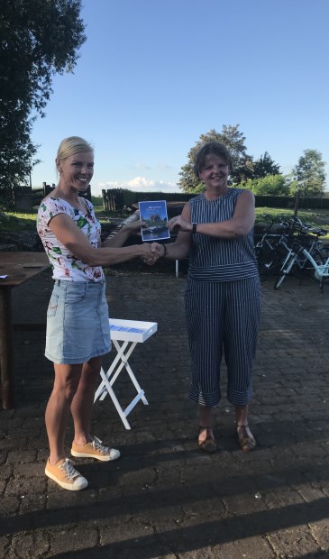 Wethouder Paula Jorritsma krijgt het eerste boekje 'Woudrichem Stroomt' uit handen van Daphne van Hekken van VVV Altena Biesbosch.