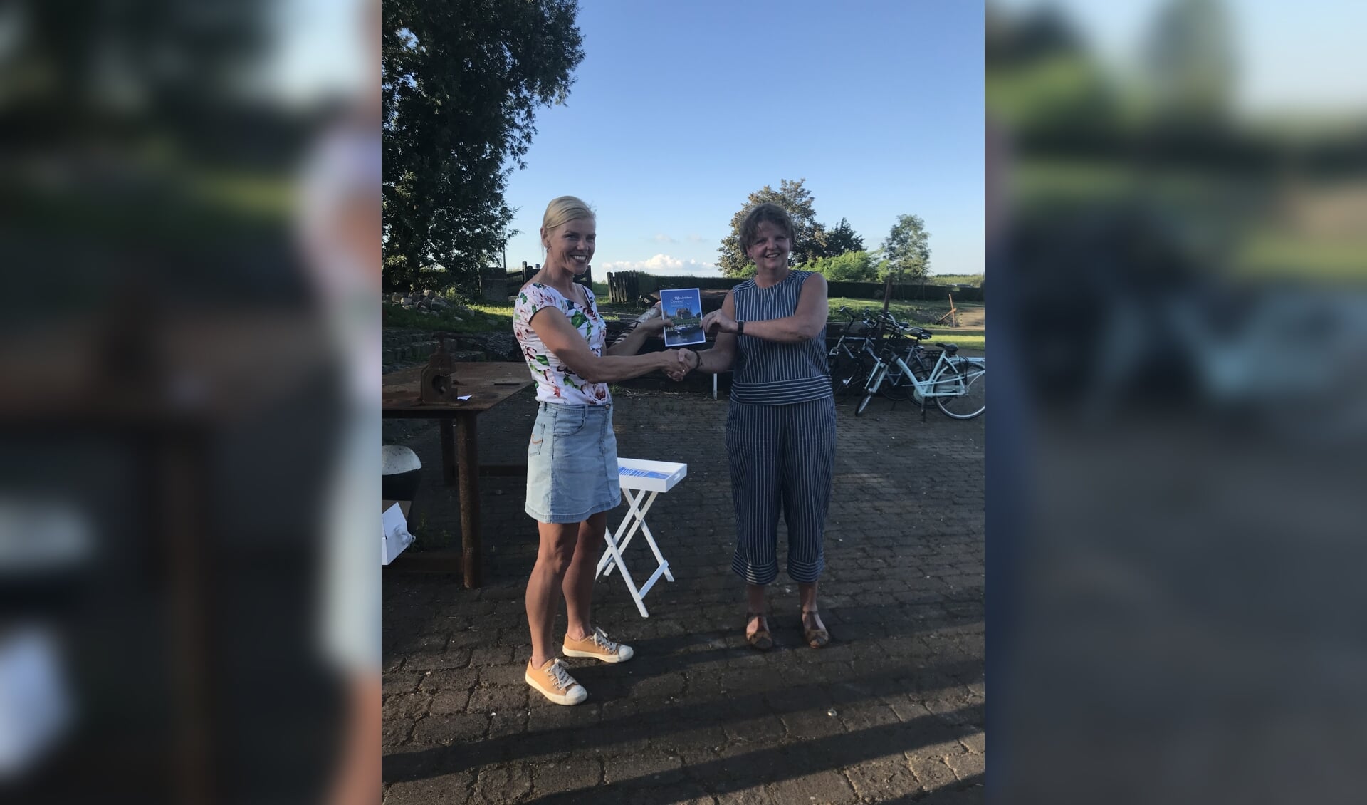 Wethouder Paula Jorritsma krijgt het eerste boekje 'Woudrichem Stroomt' uit handen van Daphne van Hekken van VVV Altena Biesbosch.