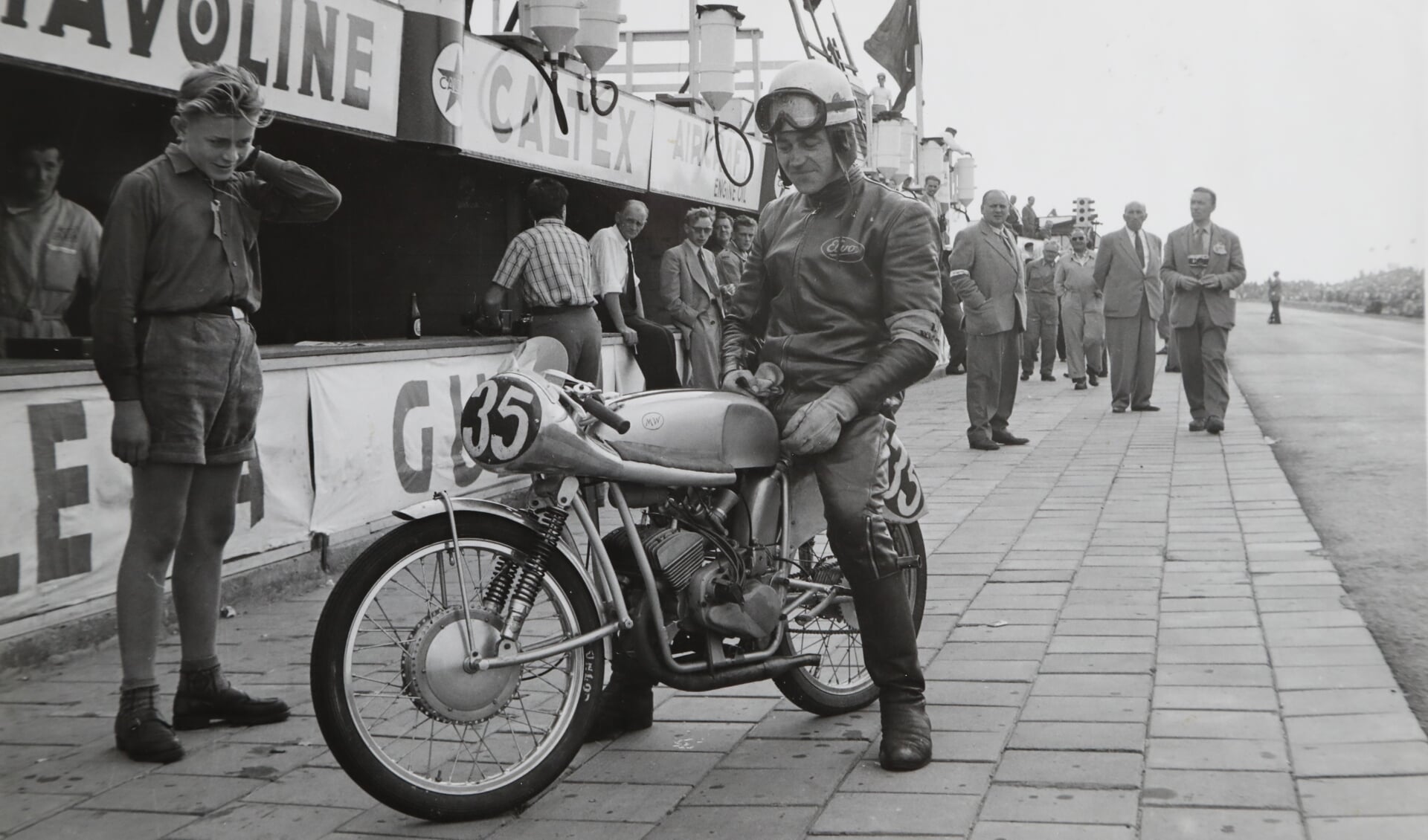 • Jan Muijlwijk op zijn zelfgebouwde motorfiets tijdens de TT races in 1954. Koen is het het jongetje in korte broek.