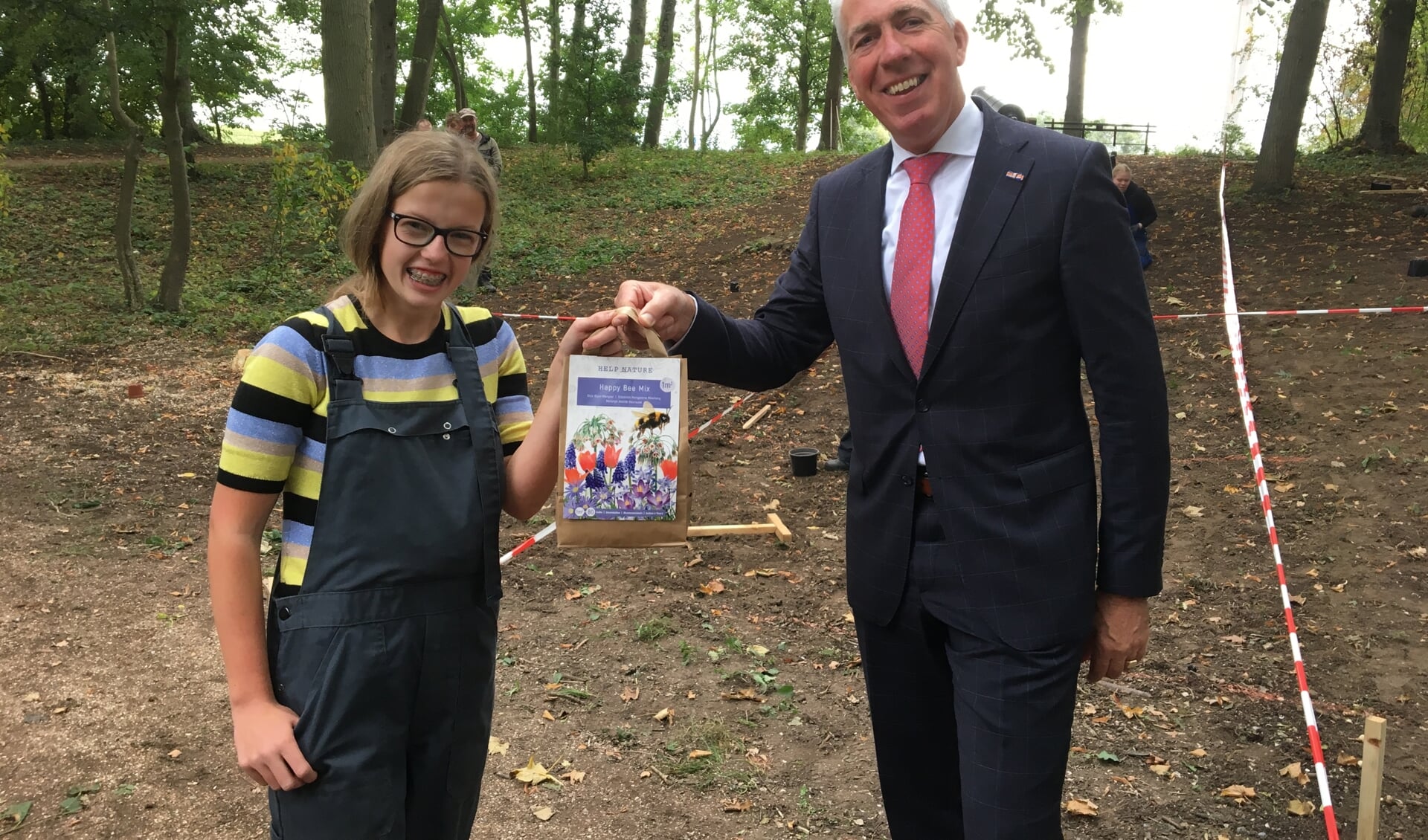 • Wethouder Gijs van Leeuwen overhandigt een zakje met bloembollen aan Tiana van Hemert uit Nieuwaal. Zij is leerling van praktijkschool De Brug.