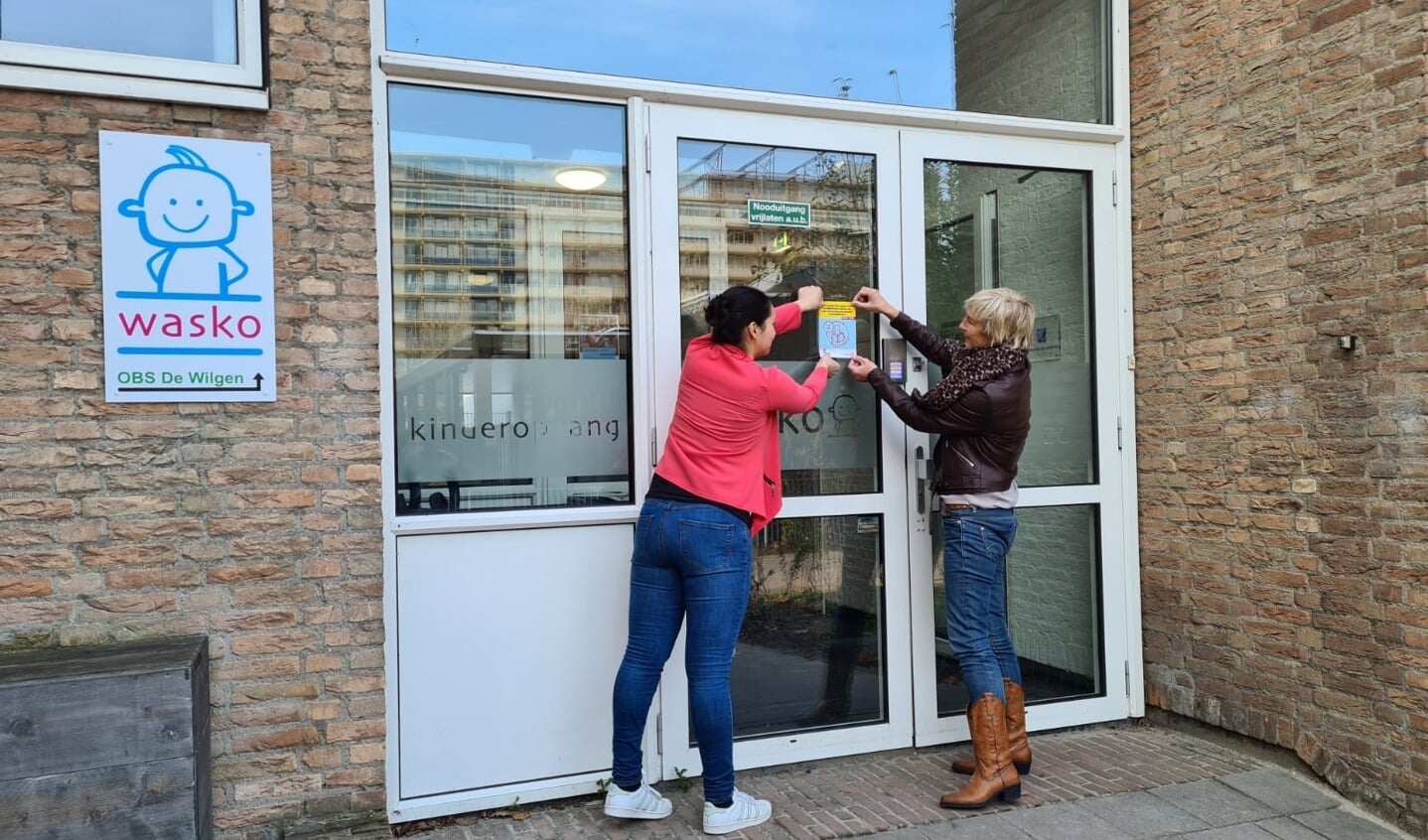 Ellen van Eijmeren (Bibliotheek AanZet) en Daisy Markesteijn (Wasko Kinderopvang) plakken trots het keurmerk Boekstart op de ramen.