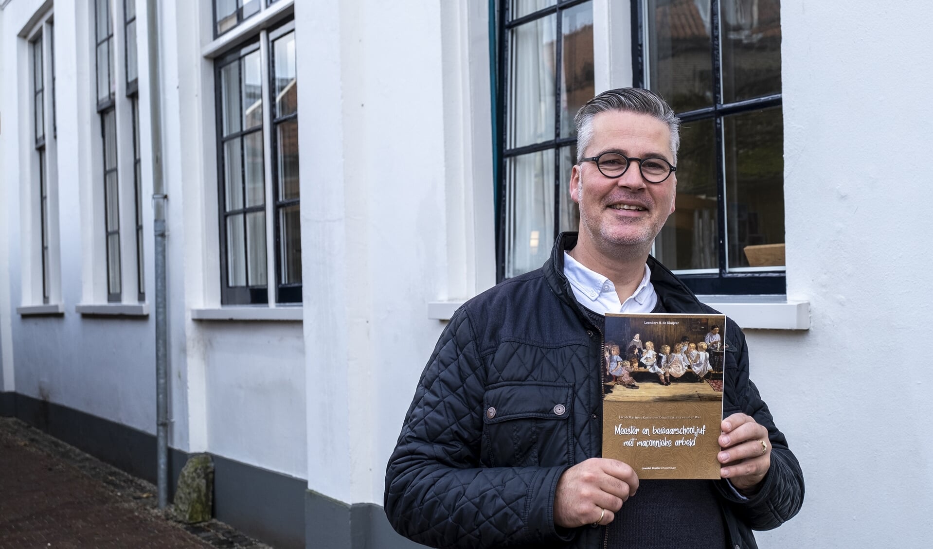 • Leo de Kluijver met zijn boek voor het Thomashuis, waar vroeger de 'bewaarschool' was gevestigd.