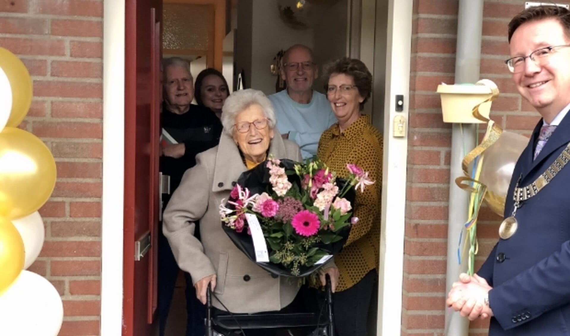 Omringd door haar kinderen ontvangt mevrouw Walschots de burgemeester aan de deur, waar ze - op afstand - ruimschoots de tijd neemt voor een gezellig praatje. (Foto: Lysette Verwegen)