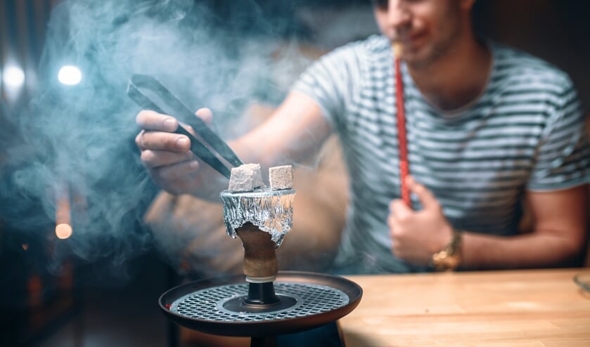Young man with tongs kindle the coal at hookah bar. Shisha tobacco smoke.