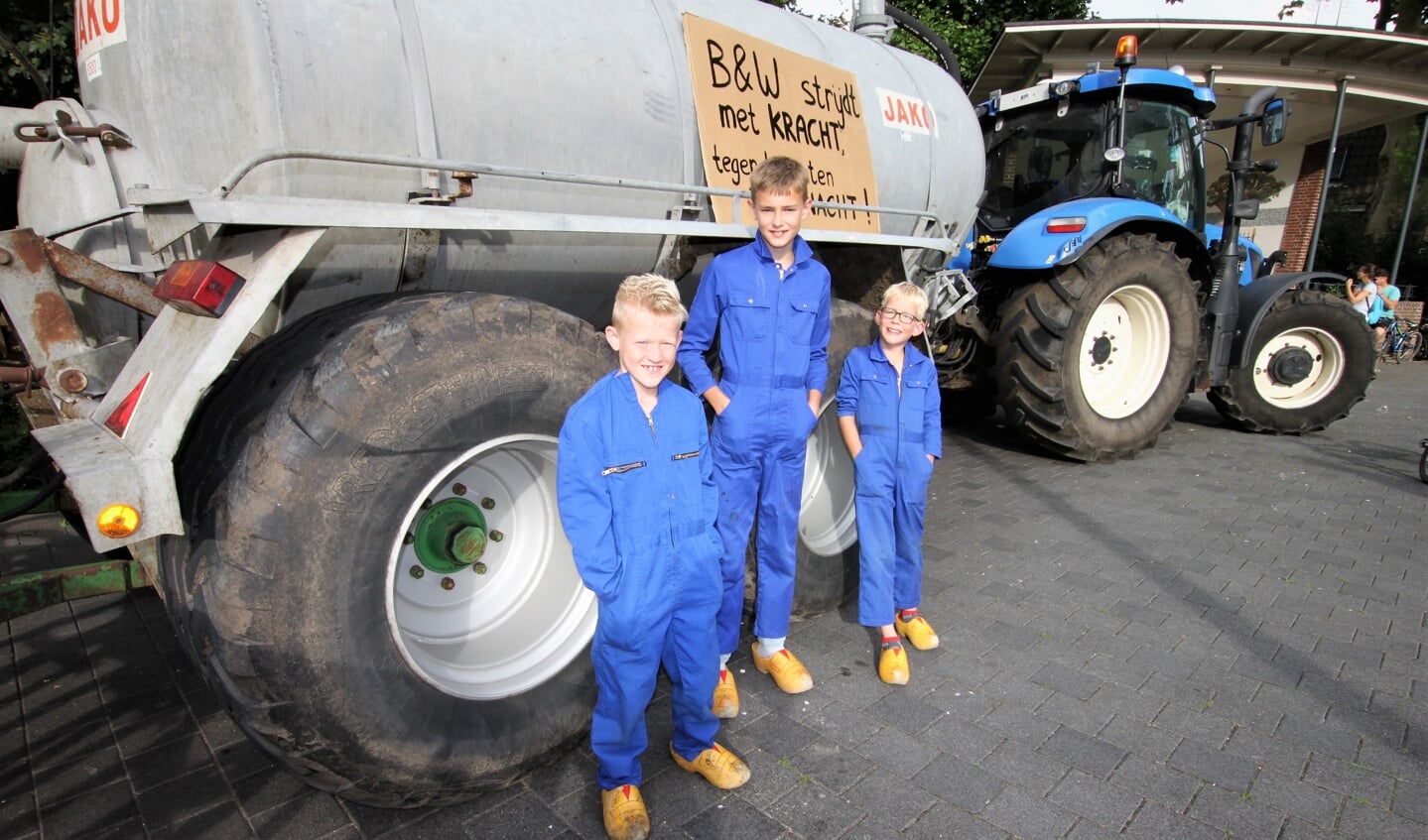 • Drie jongens in overall bij een geparkeerde tractor met mestwagen op Plantsoen de Maenstand in Ouderkerk aan den IJssel.    