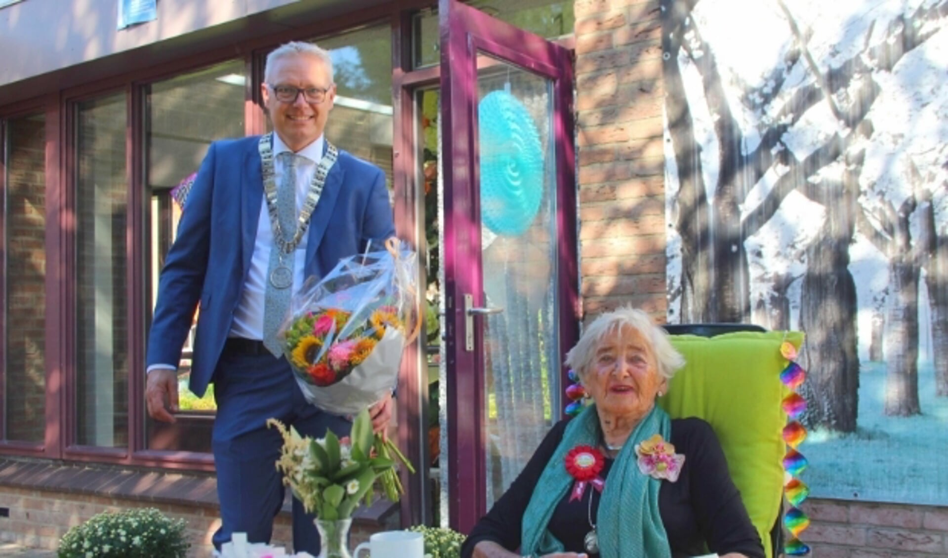 Mevrouw Buijtendijk genoot op een zonnig terras van haar honderdste verjaardag en werd ook door locoburgemeester Bekker - op gepaste afstand - in de bloemetjes gezet. (Foto: Lysette Verwegen)