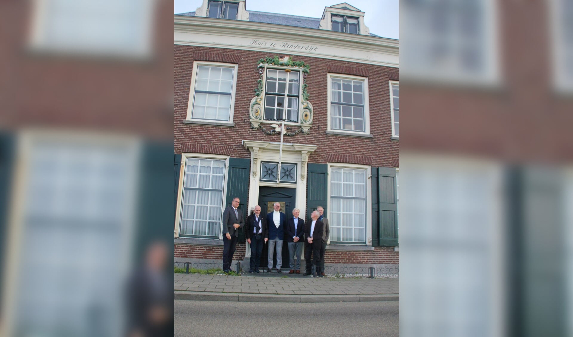 • Het stichtingbestuur met burgemeester Paans en kunstenaar Roel Teeuwen bij Huis te Kinderdijk, met het beeldje van Beatrijs in de gevel.