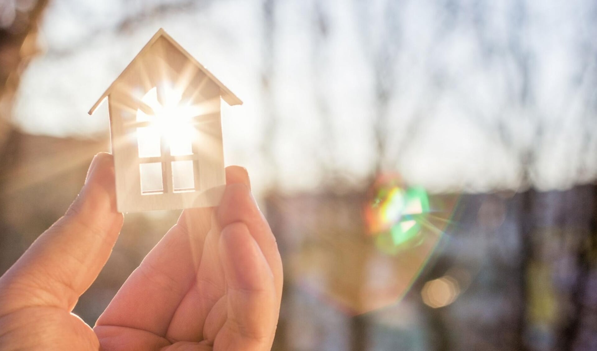 House in hand in the rays of the sun. The concept of protection of property.