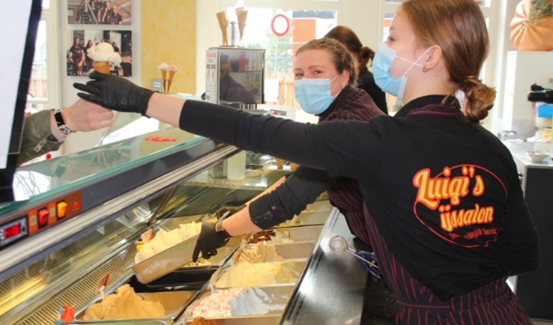 Astrid van Dijken vult de bakken in de vitrine bij met het door Chris en haar ambachtelijk gemaakte ijs. Ondertussen helpen haar medewerkers de klanten die buiten op hun beurt wachten.