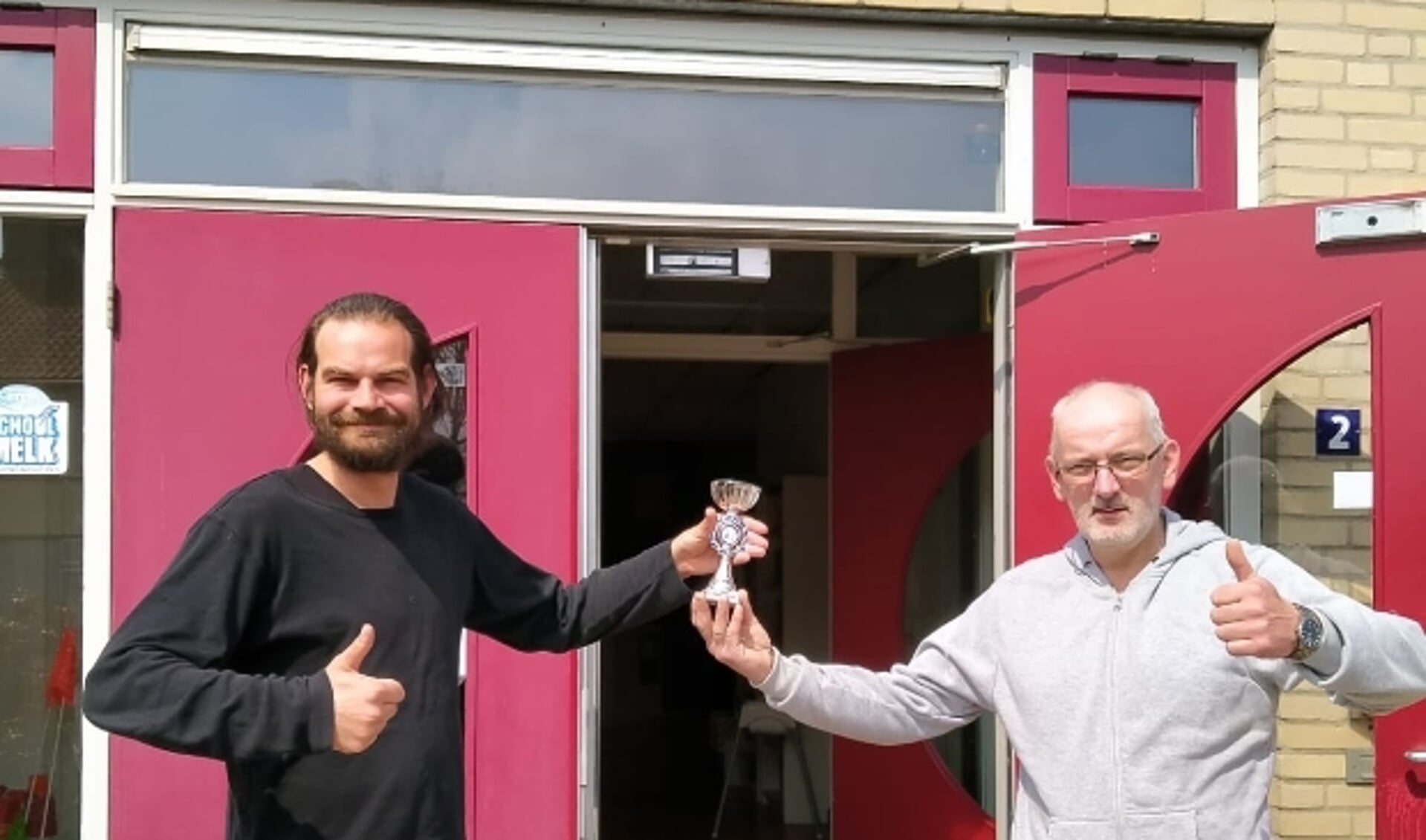 Leerkracht Hans van Tussenbroek (links) neemt namen de leerlingen van basisschool Floriant de prijs van het Digitale Burgerweeshuis Jeugdschaaktoernooi 2021 in ontvangst van organisator Dirk van Zetten van Schaakvereniging RivierenlandScha