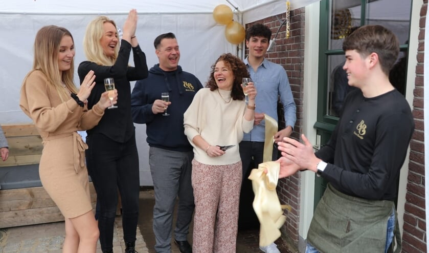 • Sabine, met schaar, heeft het lintje zojuist doorgeknipt. Op de foto staan verder haar man Sander, de dochters en schoonzoons.