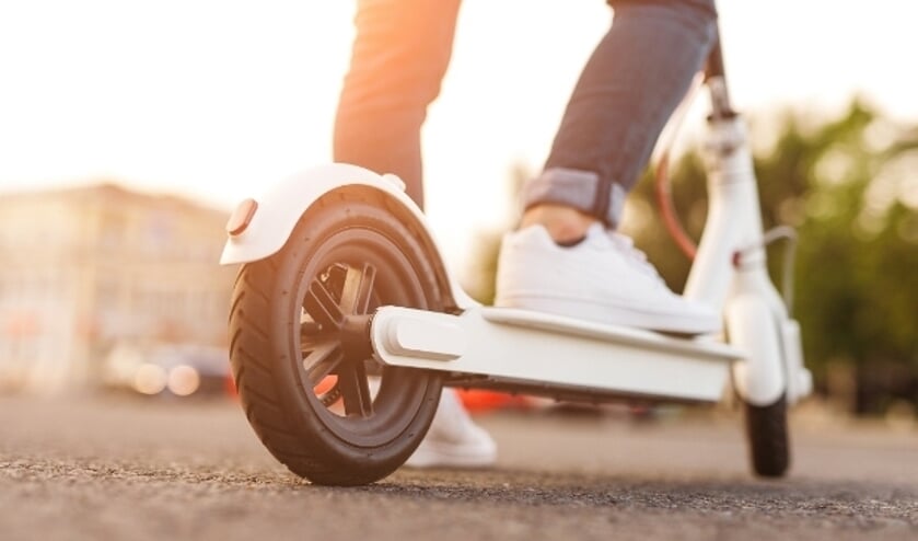 Legs of anonymous guy riding modern electric scooter on asphalt path on blurred background of city street in bright back lit