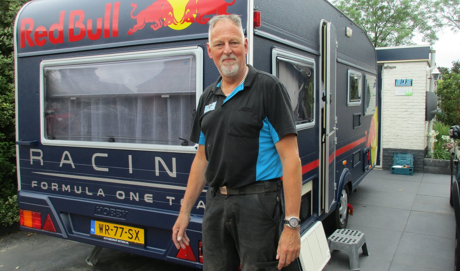 • Henk Bos bij de caravan van zoon Frank, bestickerd in het logo en de kleuren van Max Verstappen.