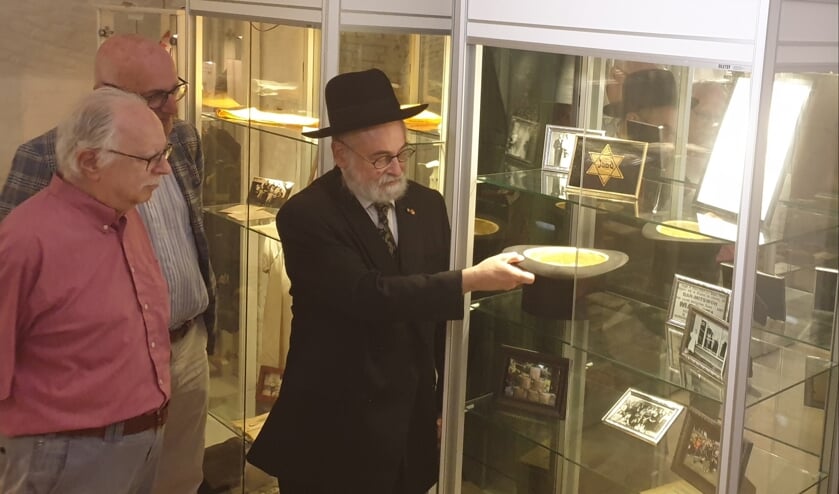 <p>Opperrabbijn Jacobs plaatst de hoge hoed van Bernard van Straten in de vitrine, onder toeziend oog van neven Harvey en Lex van Straten.</p>