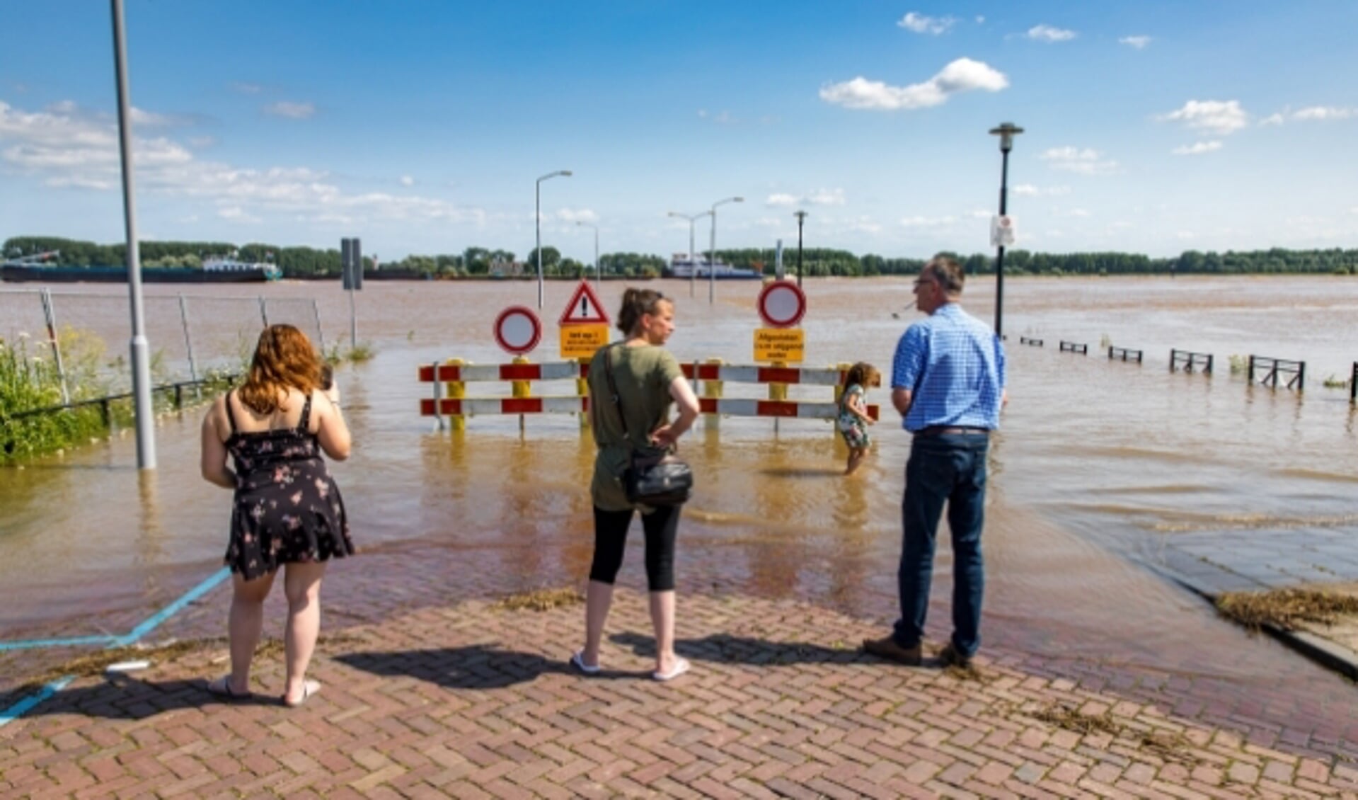 De hoge waterstand van de Waal in juli 2021 trekt veel kijkers bij de Veerweg in Tiel. De pont vaart nog. Foto Jan Bouwhuis.